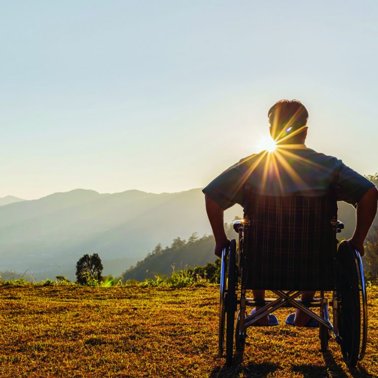 Disabled handicapped man is sitting on wheelchair at sunset.