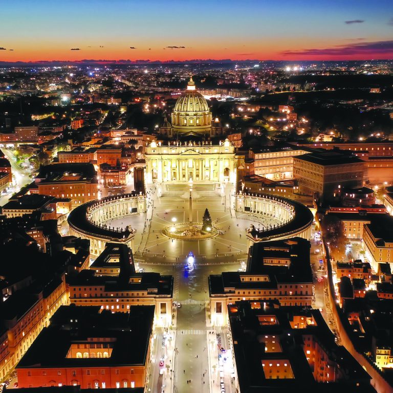 Aerial drone night shot of iconic masterpiece Saint Peter Basilica and whole illuminated city of Vatican the biggest church in the world at dusk, Metropolitan city of Rome, Italy