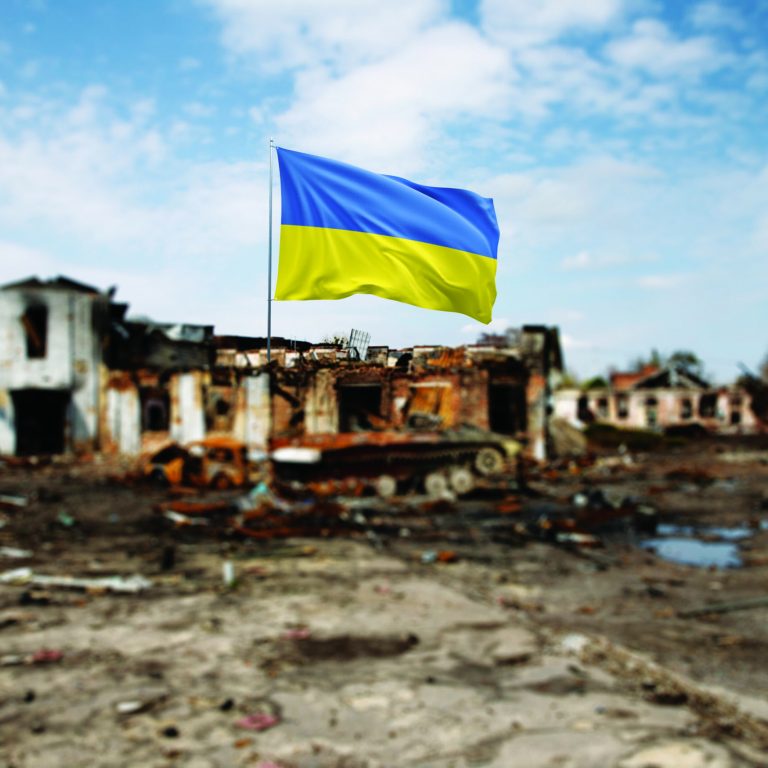 Ukrainian Flag in Front of War-Torn Ruins Under a Clear Sky