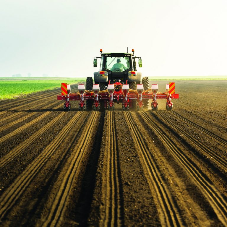 Farmer with tractor seeding - sowing crops at agricultural field. Plants, wheat.